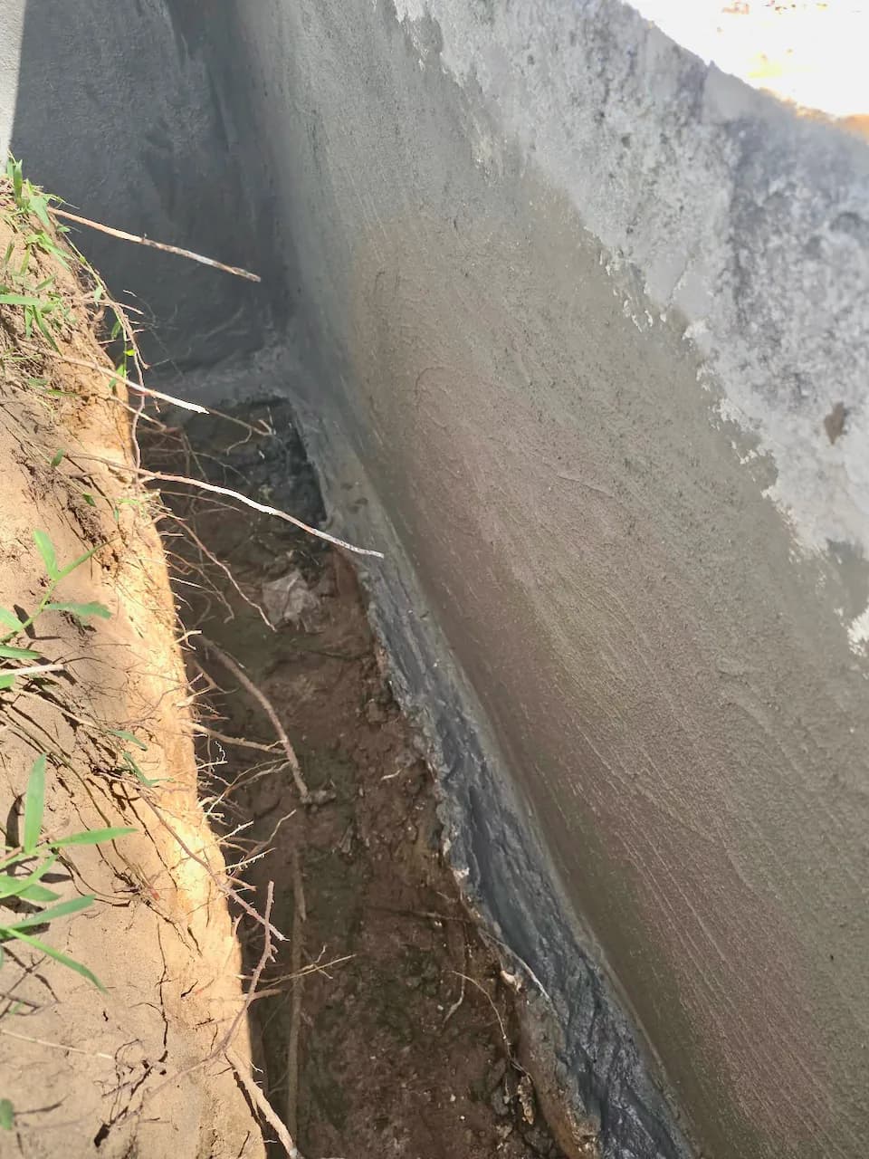 Deep trench dug along a house foundation, with the wall below ground coated in grey waterproofing Deep trench dug along a house foundation, with the wall below ground coated in grey waterproofing