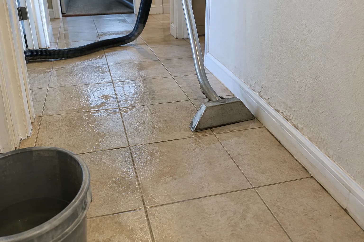 Water-extraction wand and hose on wet tile beside a swollen baseboard