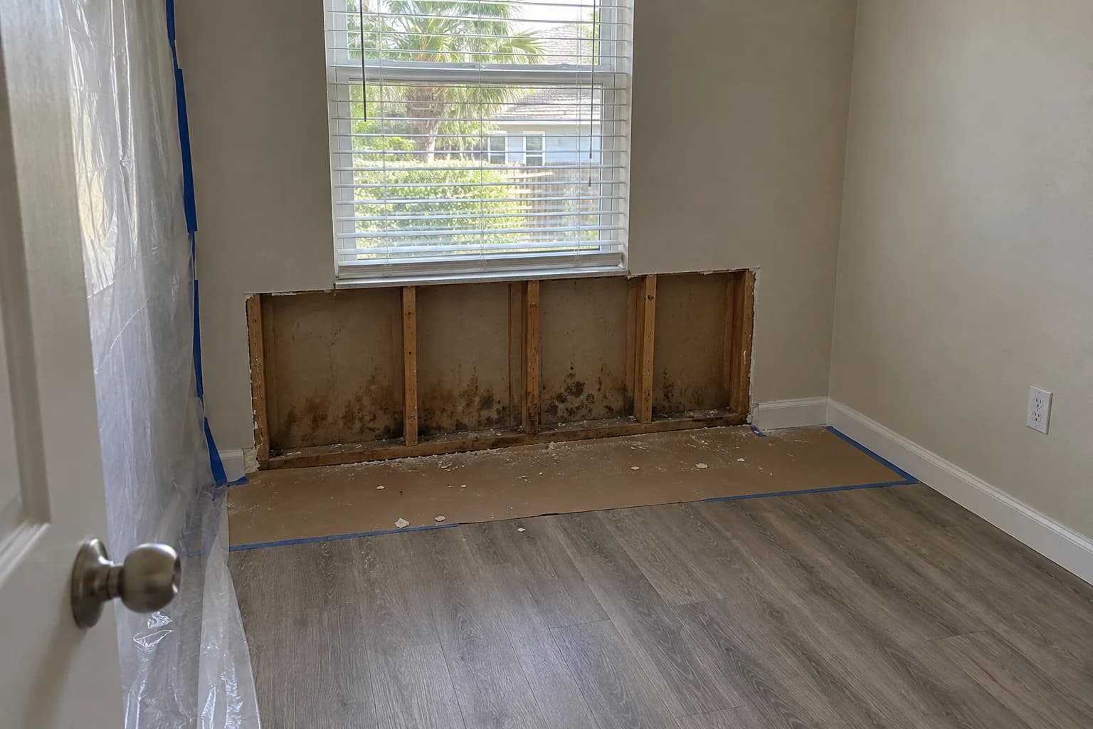 Opened wall framing beneath a window with floor protection during remediation