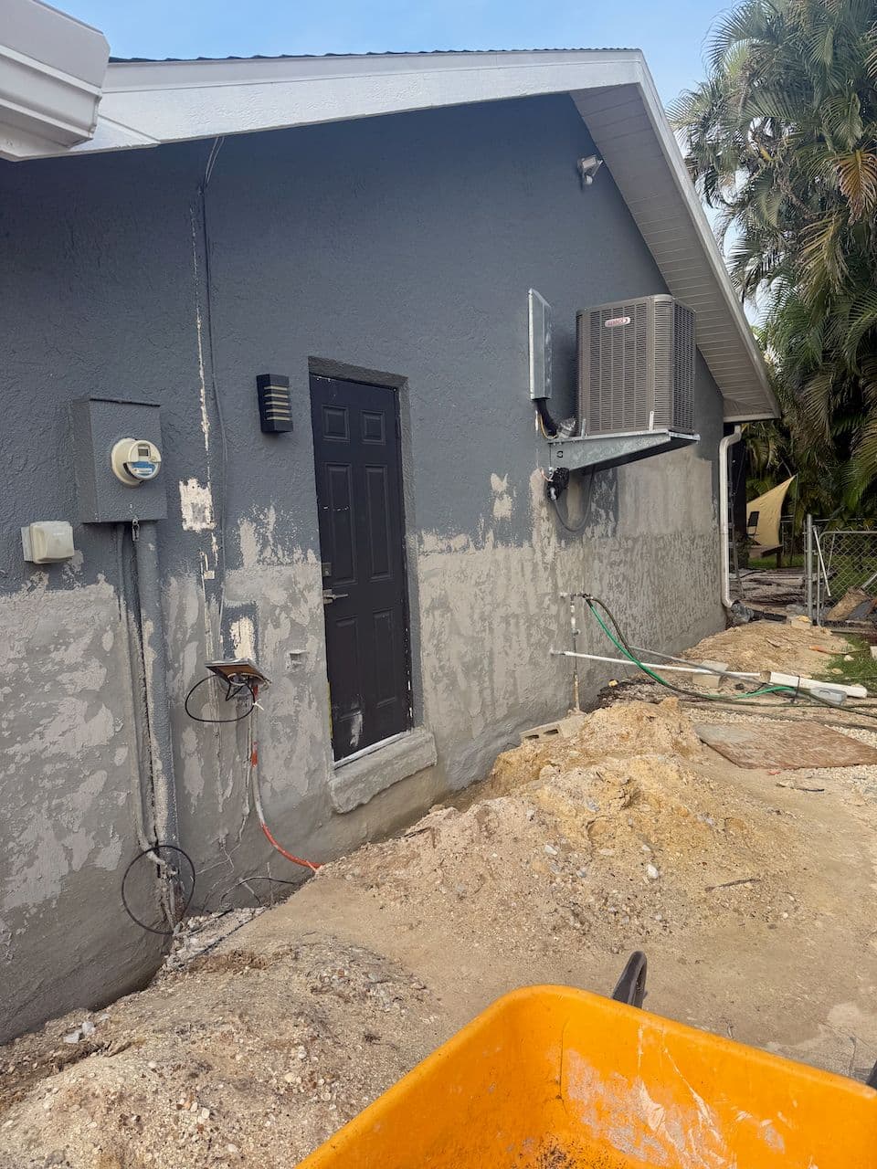 Exterior of a grey home with an exposed foundation trench and excavated dirt in preparation for waterproofing work Exterior of a grey home with an exposed foundation trench and excavated dirt in preparation for waterproofing work