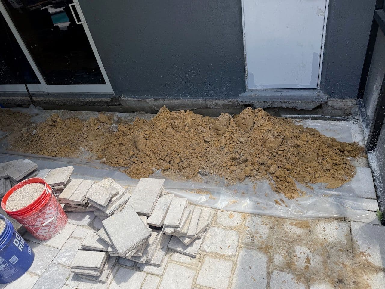 Exterior foundation trench next to a house with exposed dirt and a pile of sand near stepping stones Exterior foundation trench next to a house with exposed dirt and a pile of sand near stepping stones