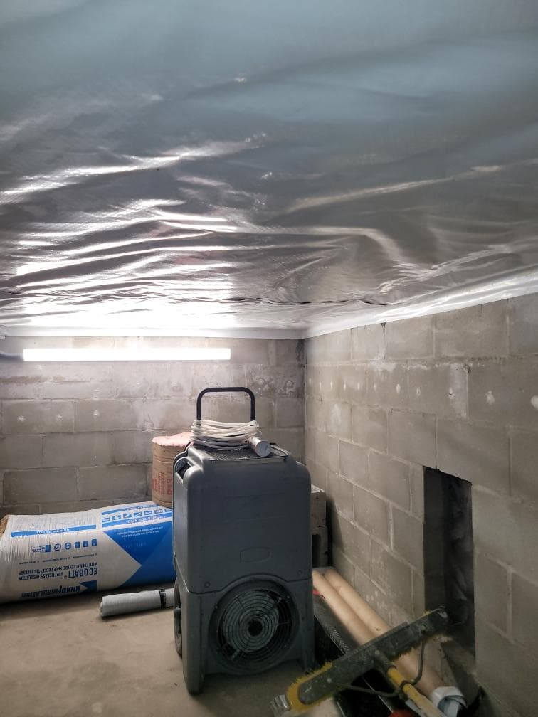 Heavy duty white plastic vapor barrier installed across the ceiling of a block wall basement with a dehumidifier and rolls of insulation below Heavy duty white plastic vapor barrier installed across the ceiling of a block wall basement with a dehumidifier and rolls of insulation below
