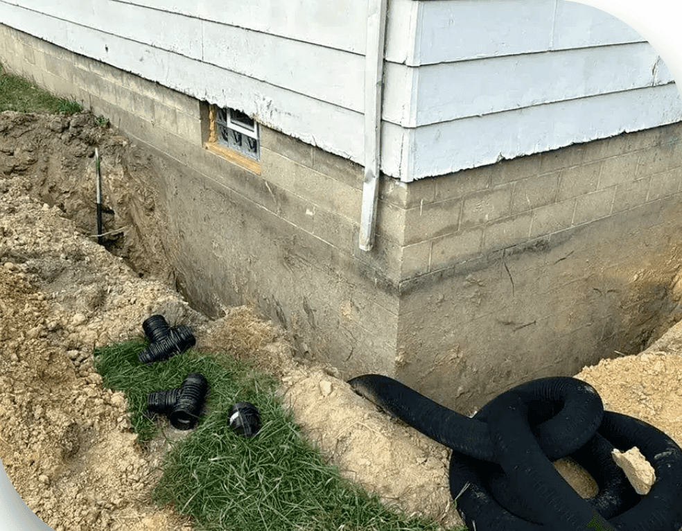 Excavated corner of a concrete block foundation wall with drainage pipe fittings prepared for waterproofing installation Excavated corner of a concrete block foundation wall with drainage pipe fittings prepared for waterproofing installation