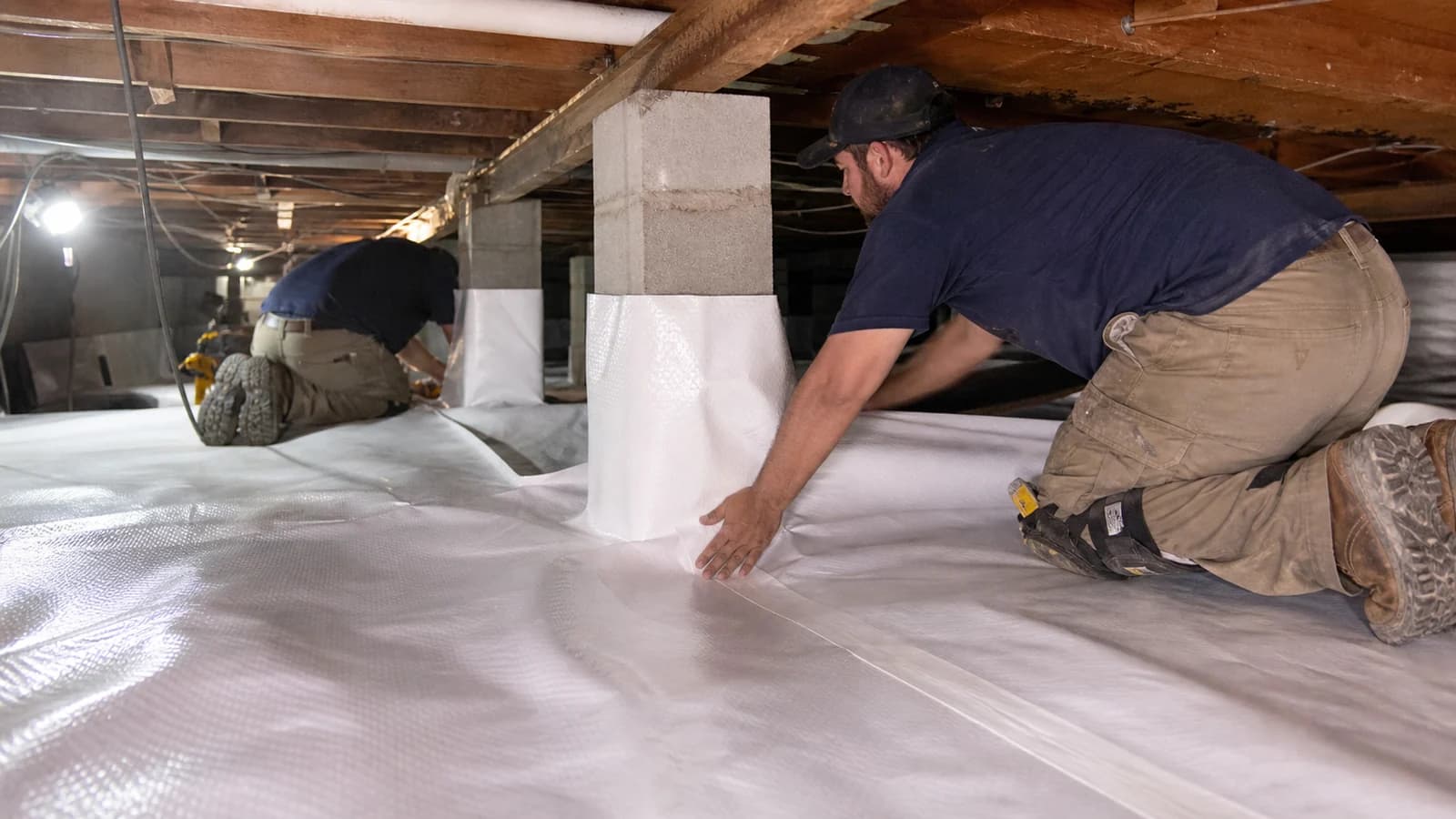 Technicians fitting reinforced white vapor barrier around a masonry pier in a low Florida crawl space Technicians fitting reinforced white vapor barrier around a masonry pier in a low Florida crawl space