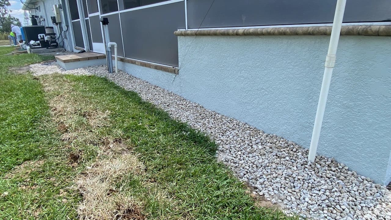 Completed exterior French drain trench filled with light grey gravel running along a house foundation Completed exterior French drain trench filled with light grey gravel running along a house foundation