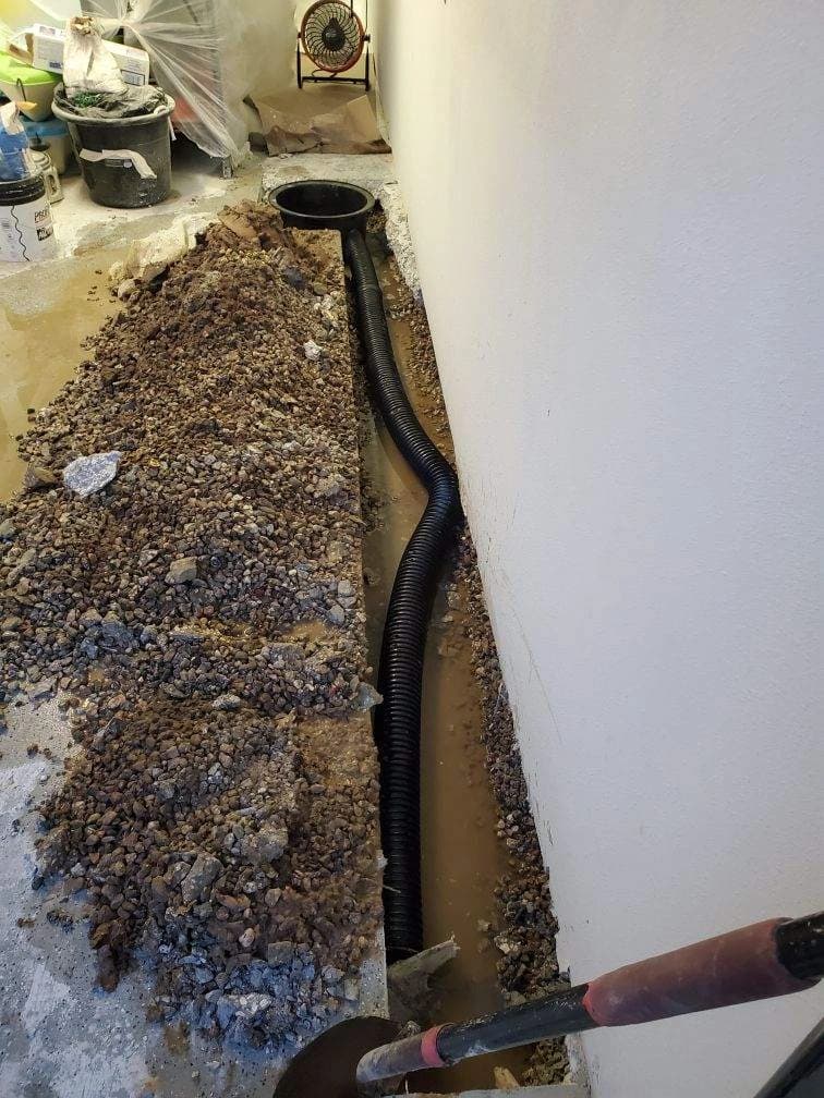 Floor cut open along an interior wall for a drain line, with gravel, corrugated pipe and water standing in the trench Floor cut open along an interior wall for a drain line, with gravel, corrugated pipe and water standing in the trench