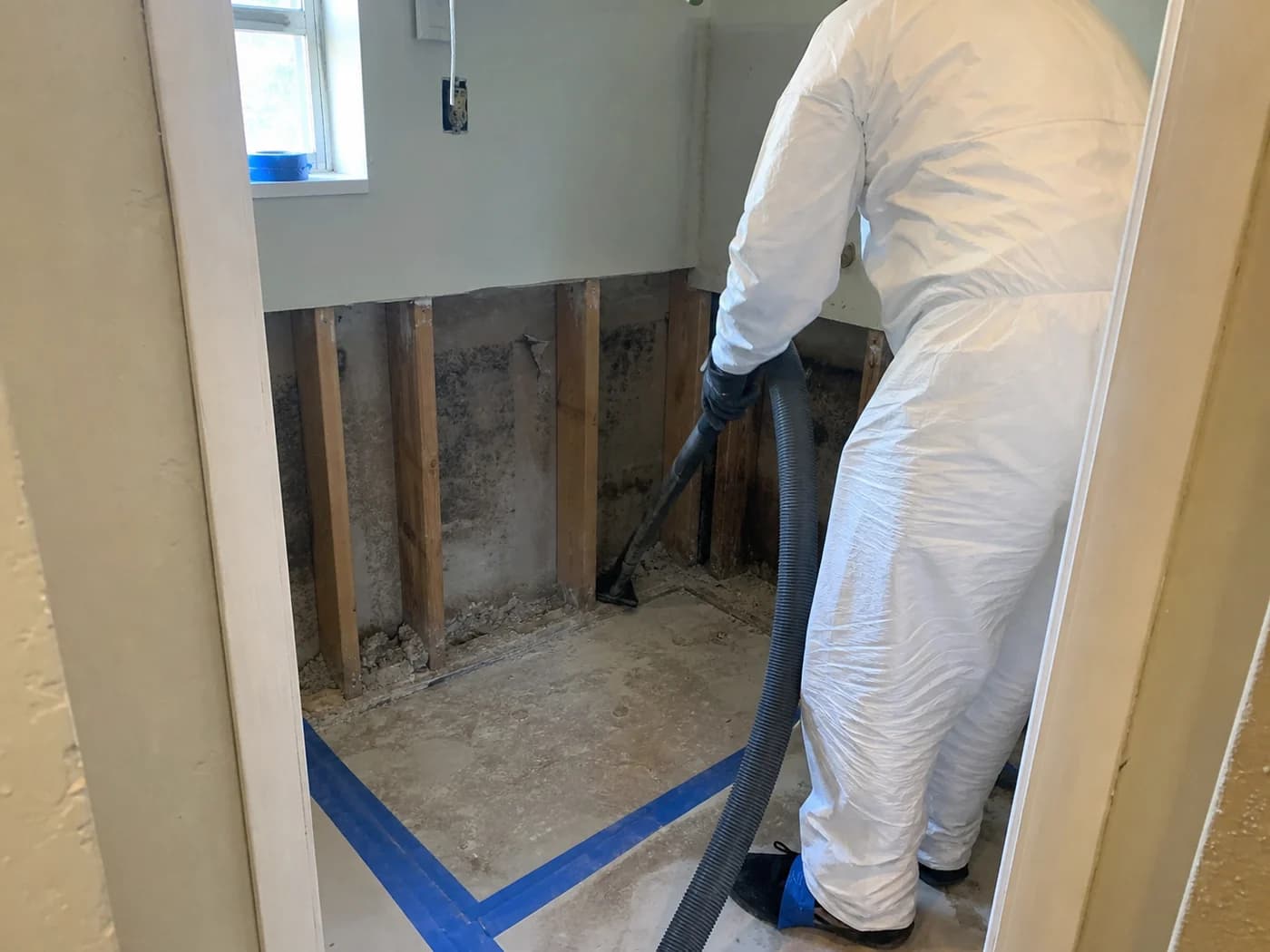 Mold remediation technician HEPA vacuuming exposed lower wall framing in an Orlando utility room Mold remediation technician HEPA vacuuming exposed lower wall framing in an Orlando utility room