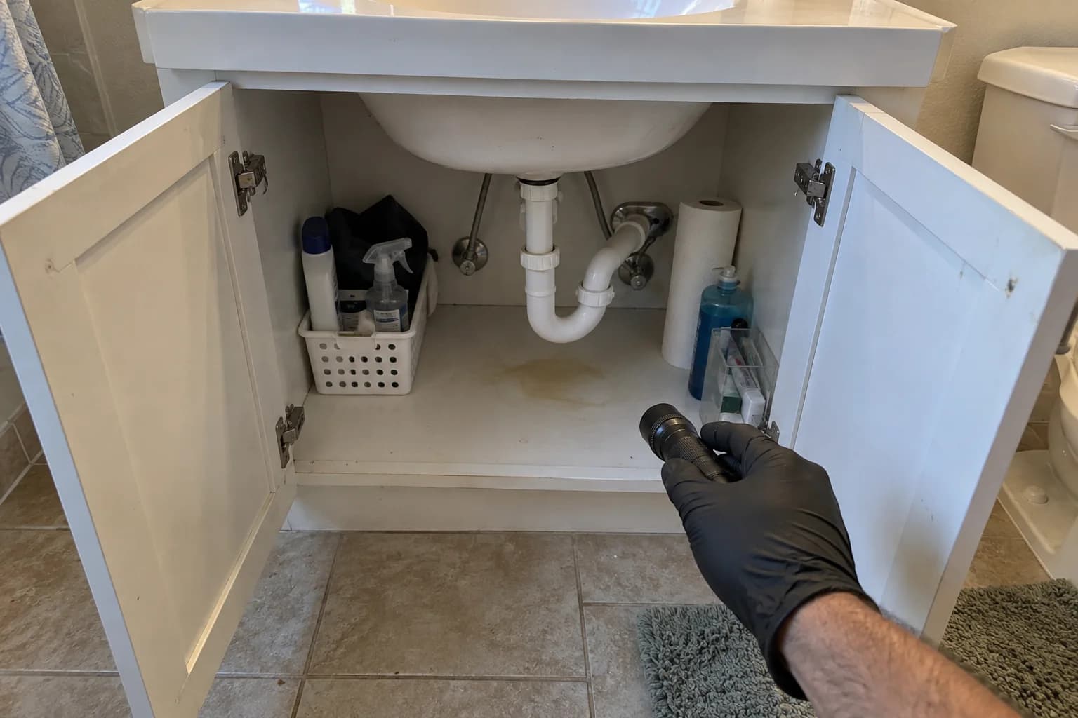 Open vanity cabinet showing plumbing and a water-stained cabinet base during an inspection Open vanity cabinet showing plumbing and a water-stained cabinet base during an inspection